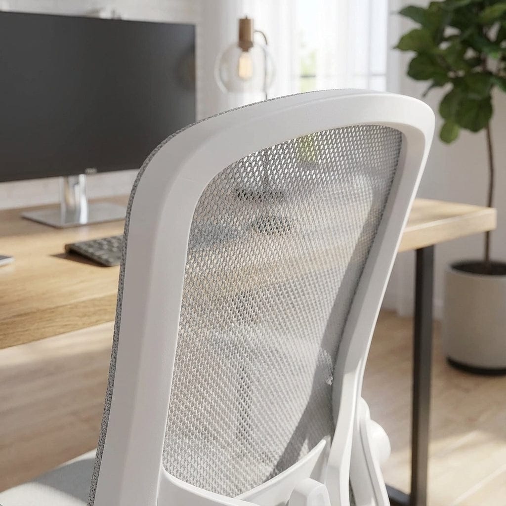 Vue rapprochée de l'arrière du dossier en maille gris clair d'une chaise de bureau ergonomique avec un cadre blanc, située dans un bureau lumineux avec un écran d'ordinateur et une plante.