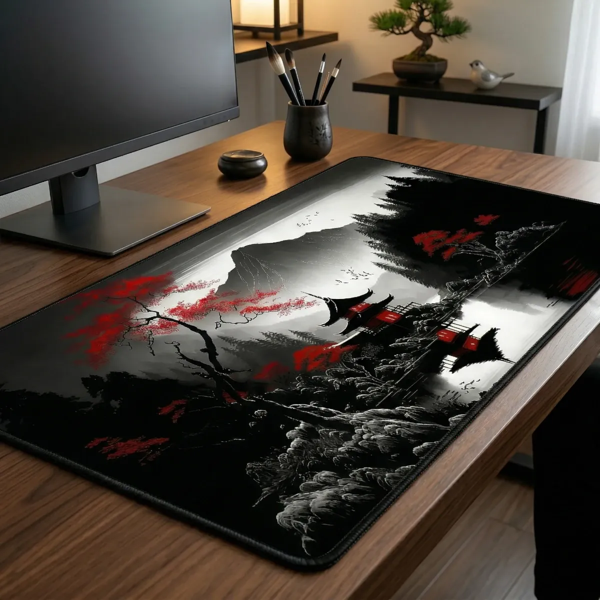 Une vue en perspective d'un setup de bureau minimaliste et zen, mettant en vedette le Tapis de souris Kurenai Ridge XXL étalé sur un bureau en bois de noyer. Le tapis affiche son design détaillé de paysage japonais en noir et blanc avec des cerisiers en fleurs rouges, entouré d'objets décoratifs zen comme un bonsaï, un pot de pinceaux et un écran d'ordinateur.
