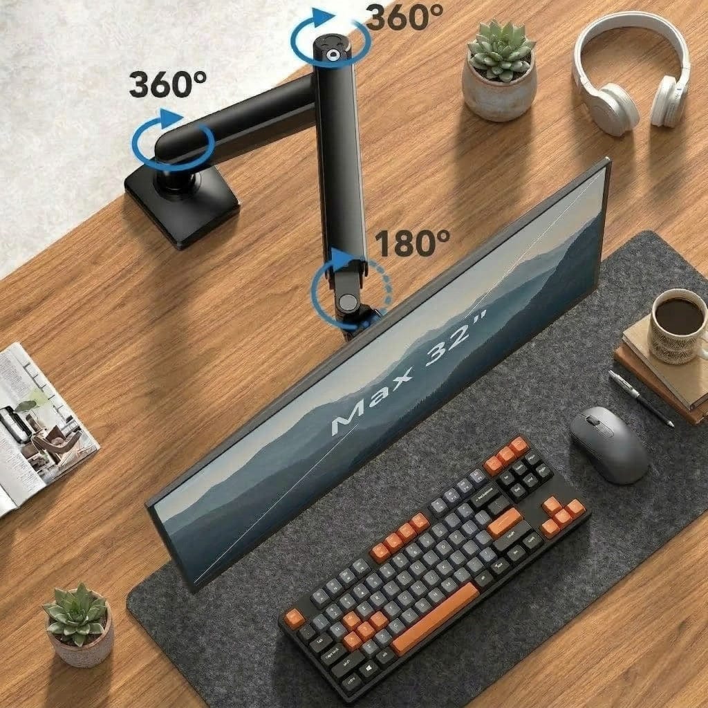 Photographie en vue de dessus d'un bras articulé noir mat fixé sur un bureau en bois brun chaleureux. Le bras supporte un écran large affichant un paysage de montagne. Des icônes bleues indiquent des rotations de 360° et 180°. Sur le bureau, on voit un clavier mécanique à touches orange et noires, une souris grise, un tapis de souris en feutre gris, une tasse de café et un casque audio blanc.