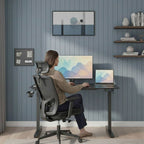 Femme assise confortablement sur une chaise de bureau ergonomique noire, travaillant sur le bureau assis-debout électrique noir réglé en position basse, vue de trois-quarts dos dans un bureau aménagé