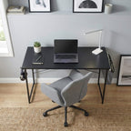 Vue d'ensemble d'un poste de télétravail avec le bureau bois MDF noir, une chaise de bureau grise et un tapis en jute.