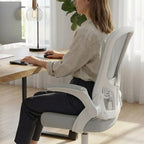 Femme utilisant un clavier à un bureau en bois, assise sur une chaise de bureau ergonomique maille grise et blanche.