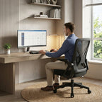 Un homme est assis et travaille à un bureau à domicile moderne sur une chaise de bureau ergonomique noire en maille. L'espace de travail est lumineux, minimaliste, avec un tapis en jute, des étagères et une fenêtre. Illustre le télétravail confortable et productif.