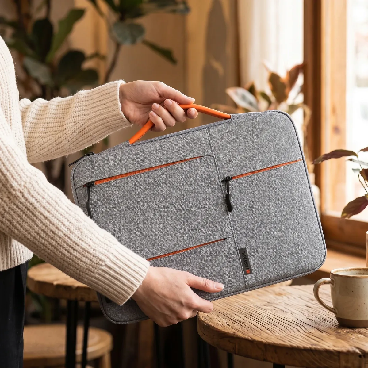 Housse ordinateur Nomad-Stretch gris portée à deux mains dans un salon