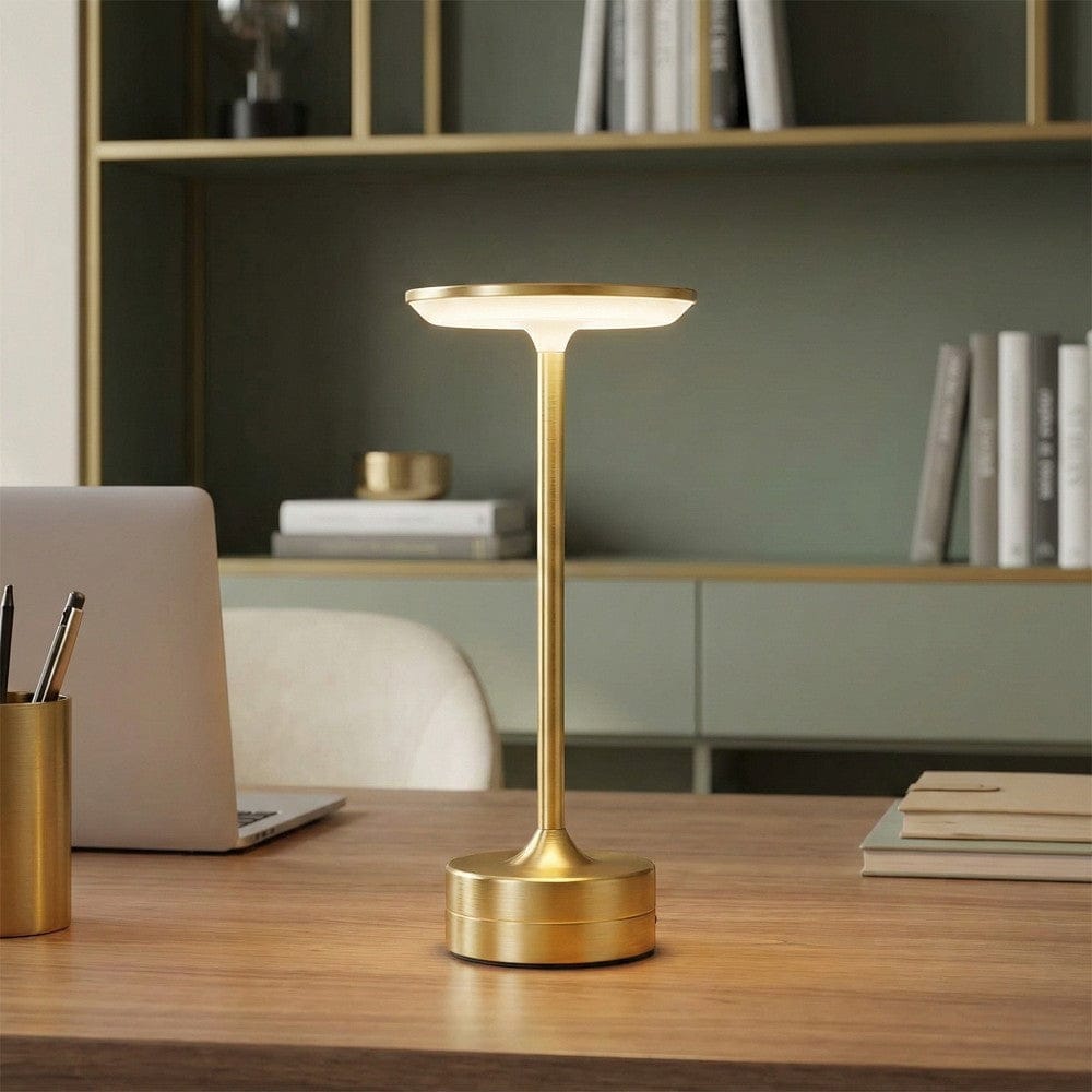 Vue rapprochée de la lampe de bureau LUXOR Liberté Absolue en finition dorée devant une bibliothèque élégante.