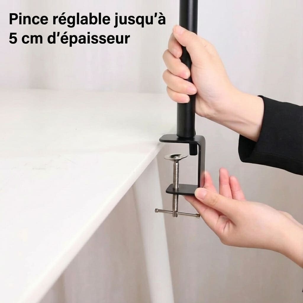 Une main installe une pince de serrage noire en forme de C sur le bord d'un bureau blanc. La pince est fixée à la base d'un support tubulaire noir. En haut à gauche, un texte en français indique : « Pince réglable jusqu’à 5 cm d’épaisseur ».