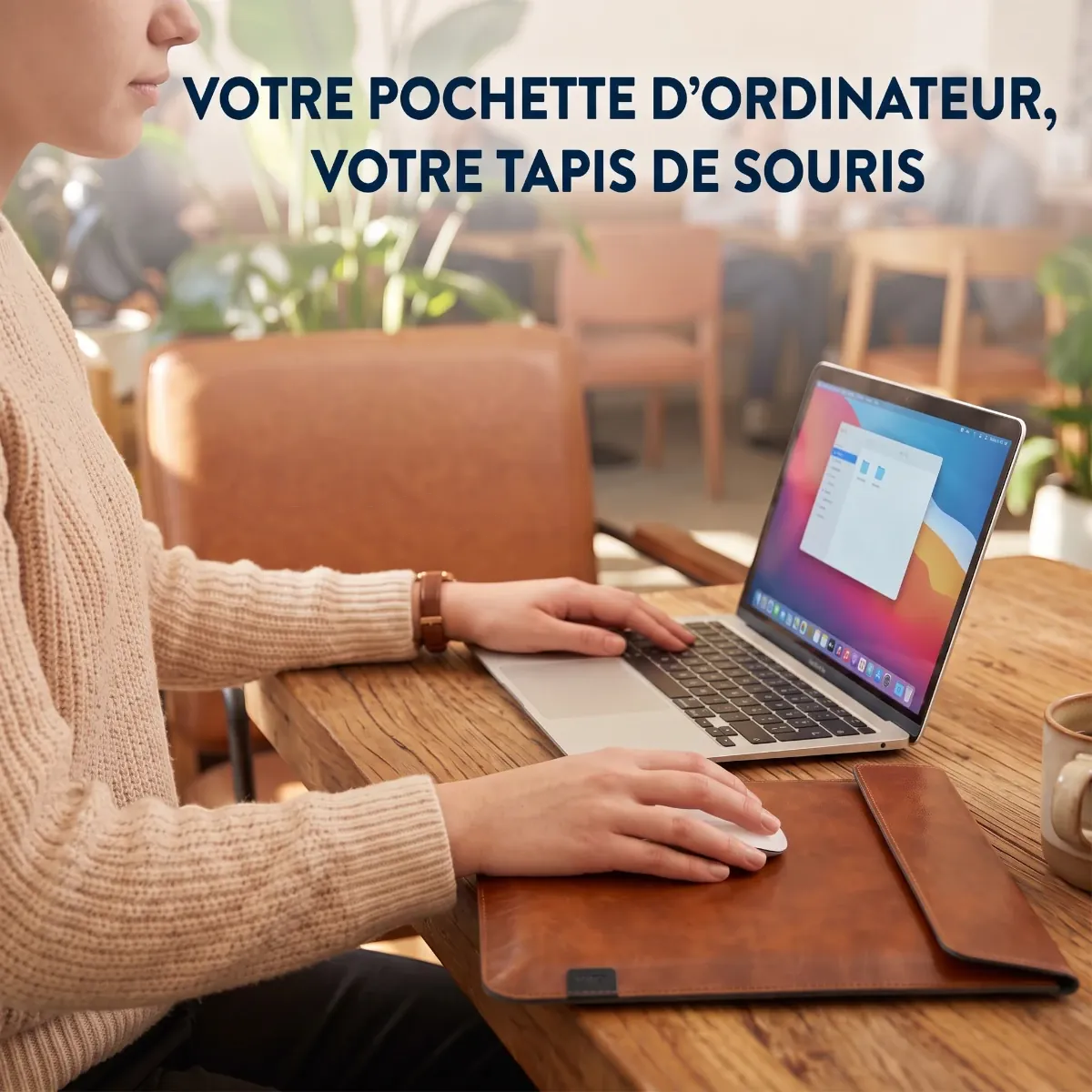 Une femme travaille sur son ordinateur portable dans un café. Sa pochette d'ordinateur en cuir marron est ouverte sur la table en bois et sert de tapis de souris pratique. En haut de l'image, le texte dit : VOTRE POCHETTE D'ORDINATEUR, VOTRE TAPIS DE SOURIS.