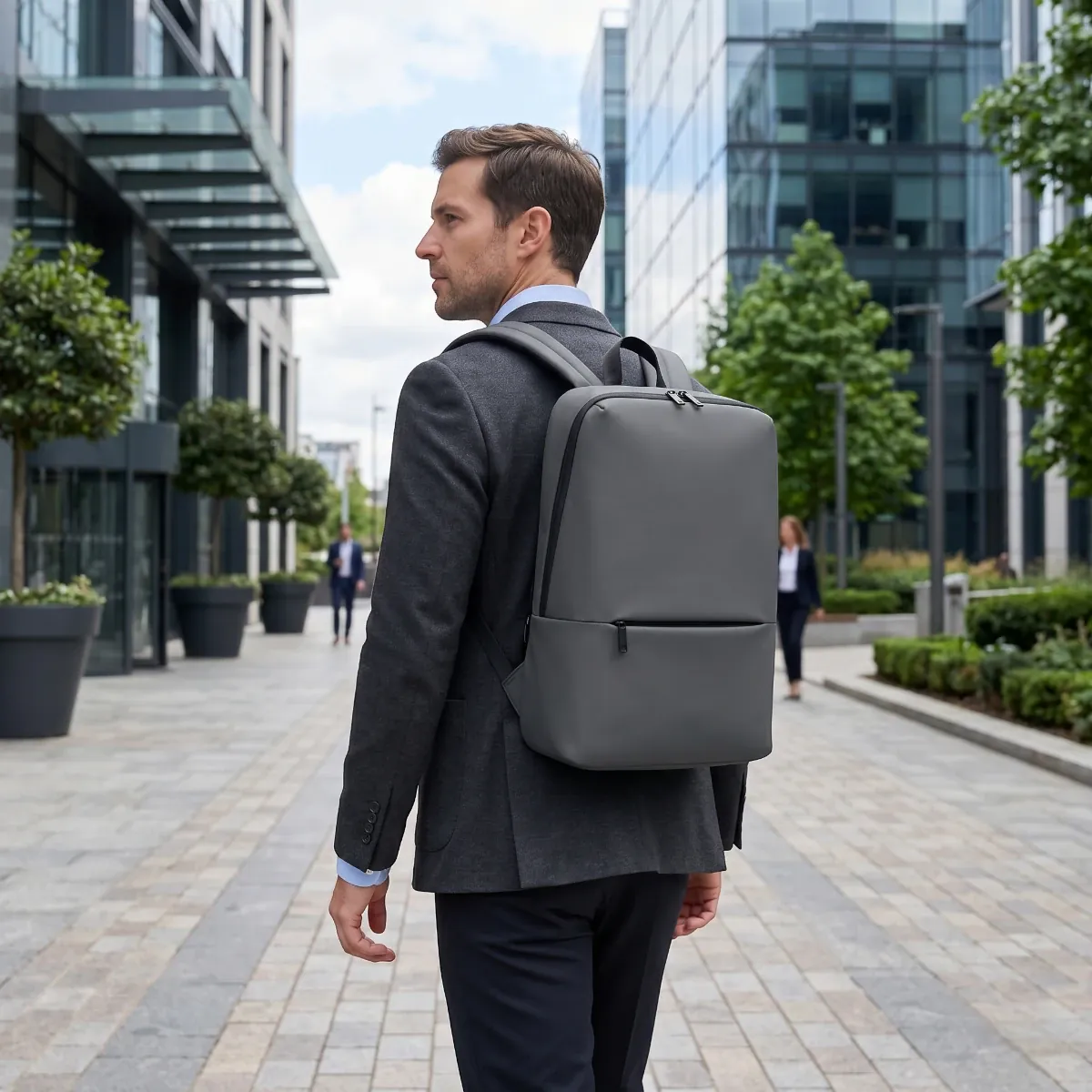Homme portant le Sac à dos ordinateur homme Classic Business V2 gris dans un quartier d'affaires moderne.