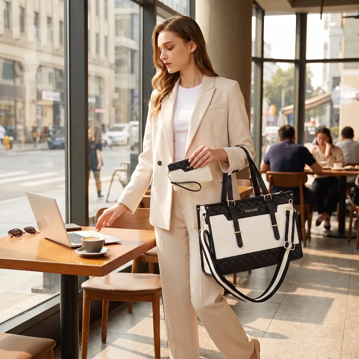 Sac ordinateur femme bicolore Gemi porté à l'épaule dans un café professionnel avec ordinateur portable et pochette assortie