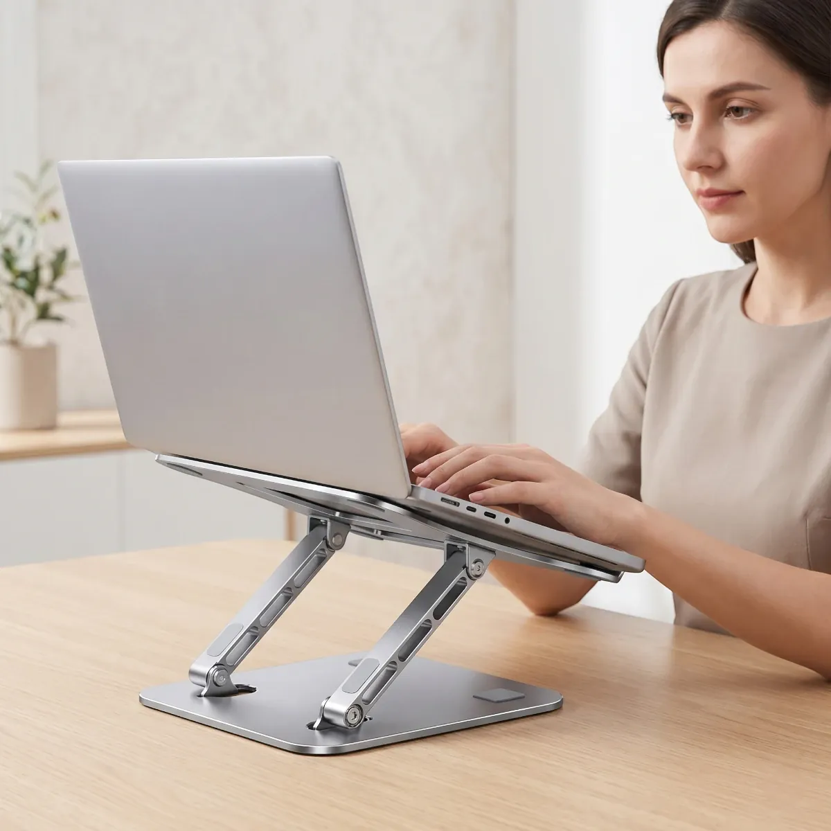 Une femme travaille sur son ordinateur portable installé sur le support AeroSteel Pro de Bureau Cosy dans un environnement style Japandi épuré.