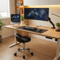 Tabouret de bureau noir à roulettes avec dossier bas placé devant un bureau assis-debout en bois.