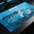 Gros plan sous un angle oblique du Tapis de souris Apex Skyline GT-R bleu clair sur un bureau noir, avec moniteur et clavier. Montre la texture micro-texturée et l'illustration GTR-R35. Format XXL.