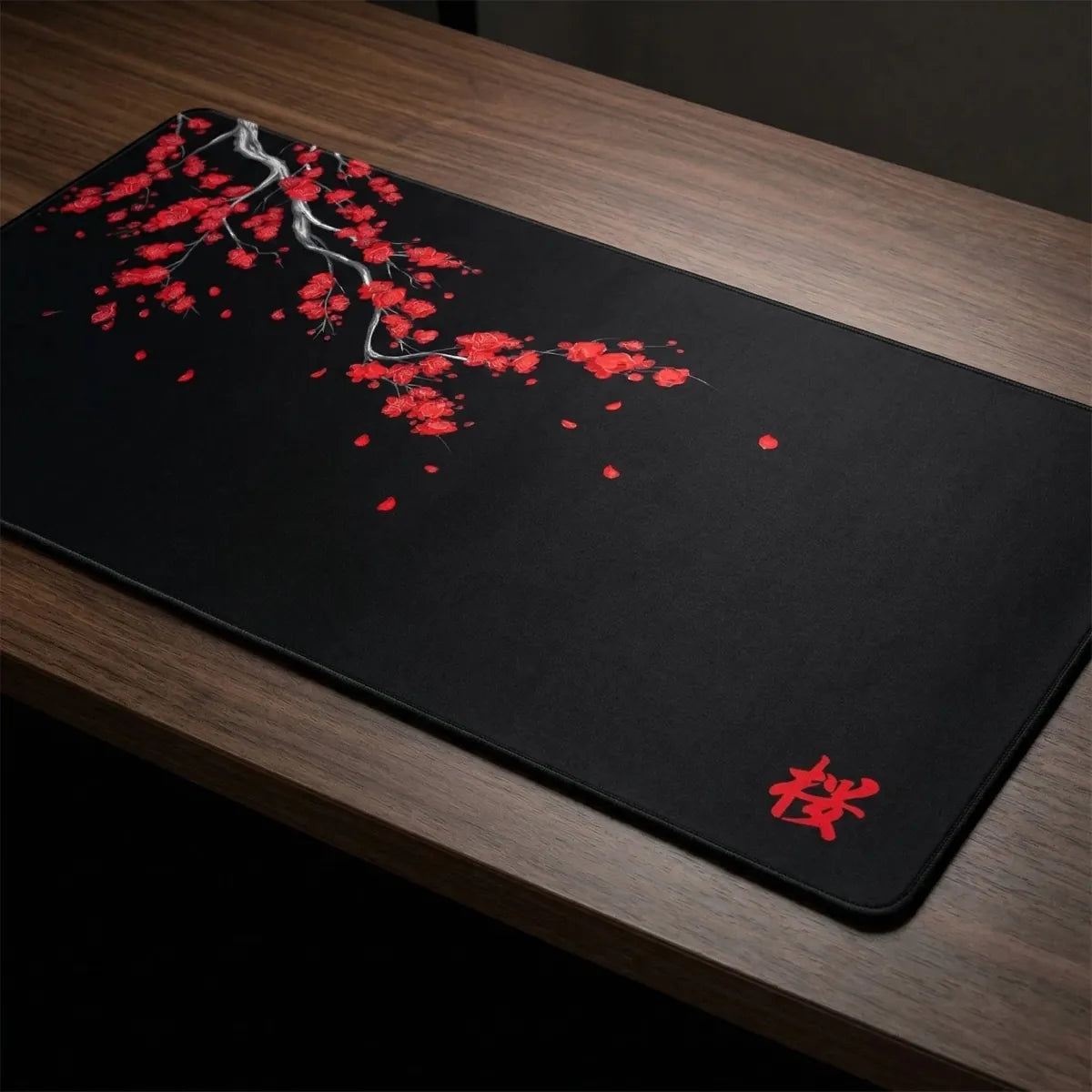 Photographie en gros plan sous un angle de trois quarts du tapis de souris Sakura Midnight XXL en tissu micro-tissé noir, révélant le motif détaillé de branche de cerisier rouge et la calligraphie kanji.